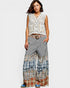Woman wearing a sleeveless floral top and patterned long skirt on a white background