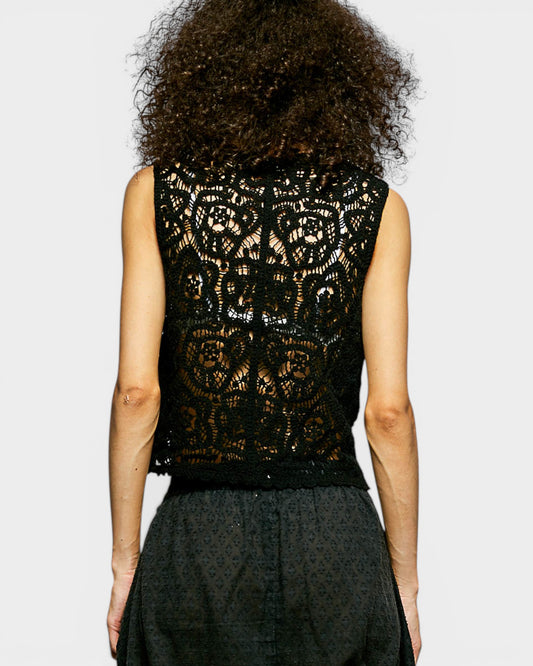 Person wearing a black lace top with a plain background