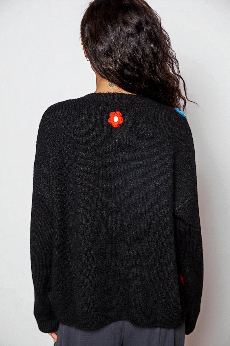 Person wearing a black sweater with a red flower design on the back against a white background