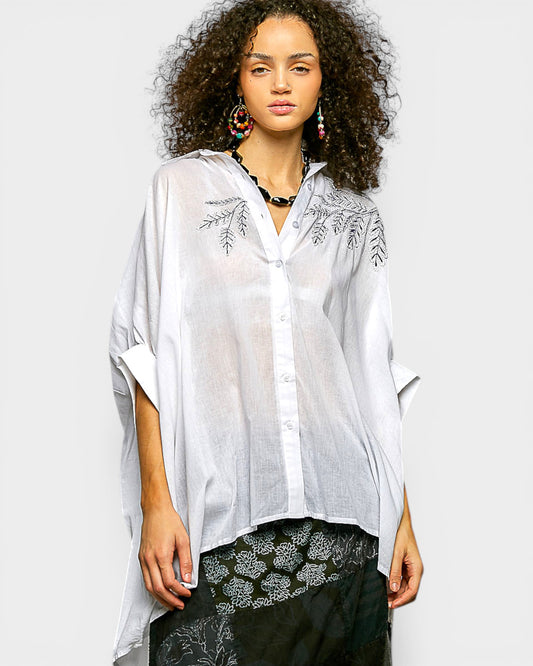 Woman wearing a white embroidered shirt over a black outfit on a plain background