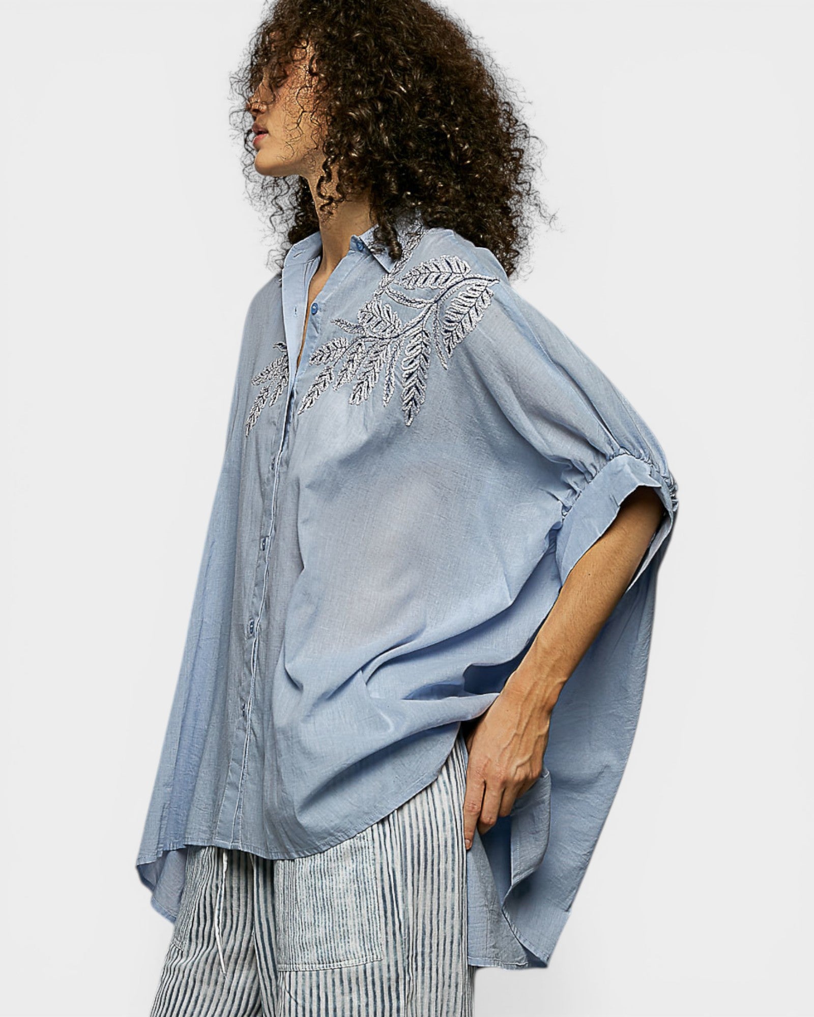 Woman wearing a light blue embroidered blouse with a plain background