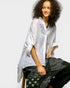 Woman wearing a white embroidered shirt with black pants on a plain background