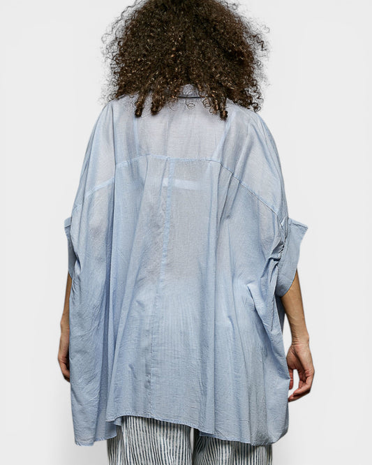 Person wearing a light blue oversized shirt on a white background