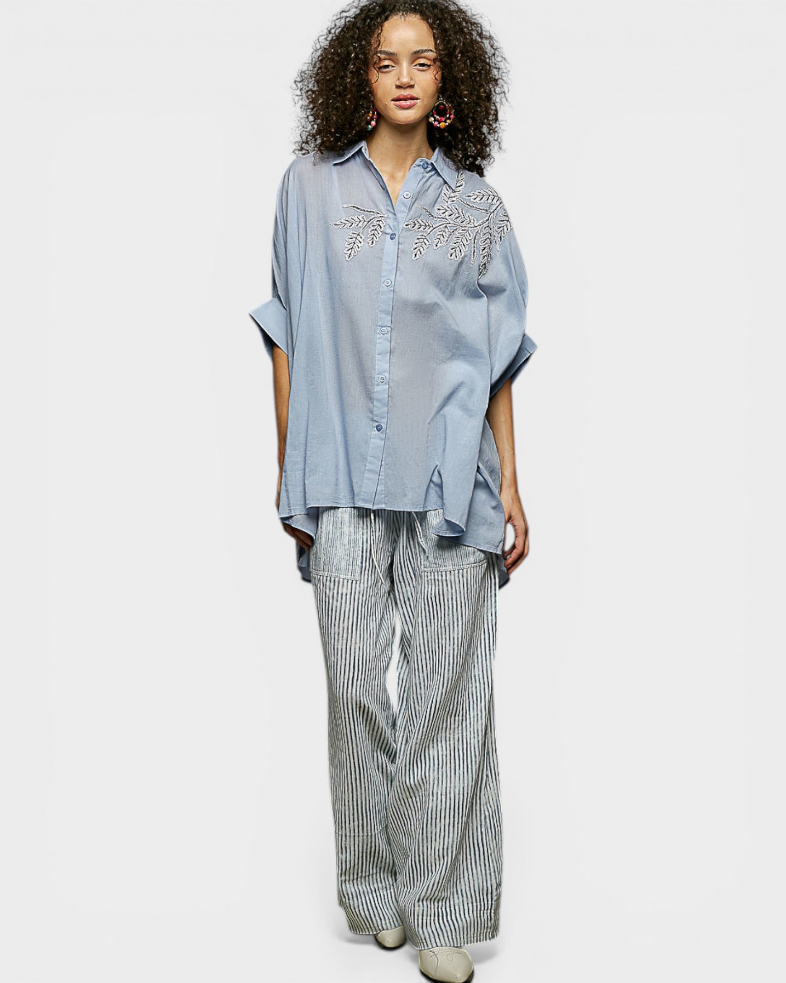 Woman wearing a light blue shirt with floral embroidery and striped pants on a white background