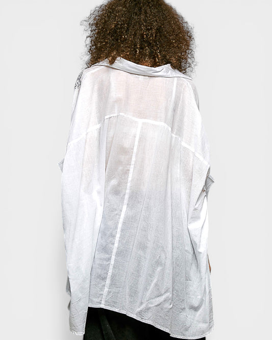 Person wearing a sheer white blouse over a black outfit on a plain background
