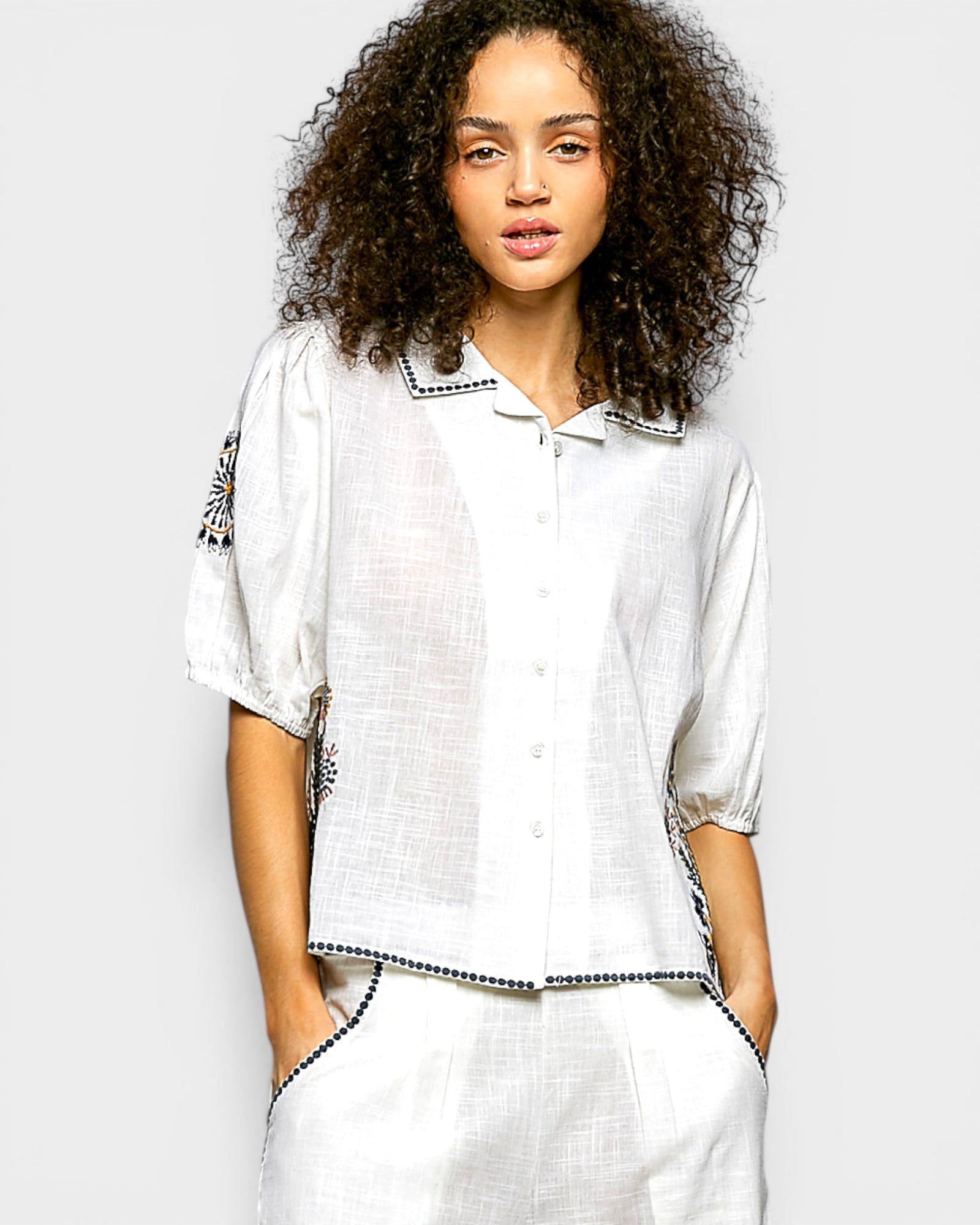Woman wearing a white outfit with black trim against a plain background