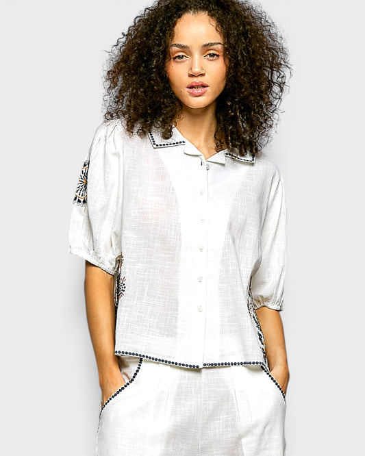 Woman wearing a white outfit with black trim against a plain background