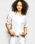 Woman wearing a white embroidered blouse and pants on a plain background
