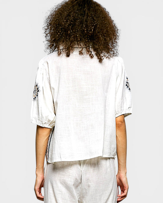 Person wearing a white outfit with black patterns on sleeves against a light gray background