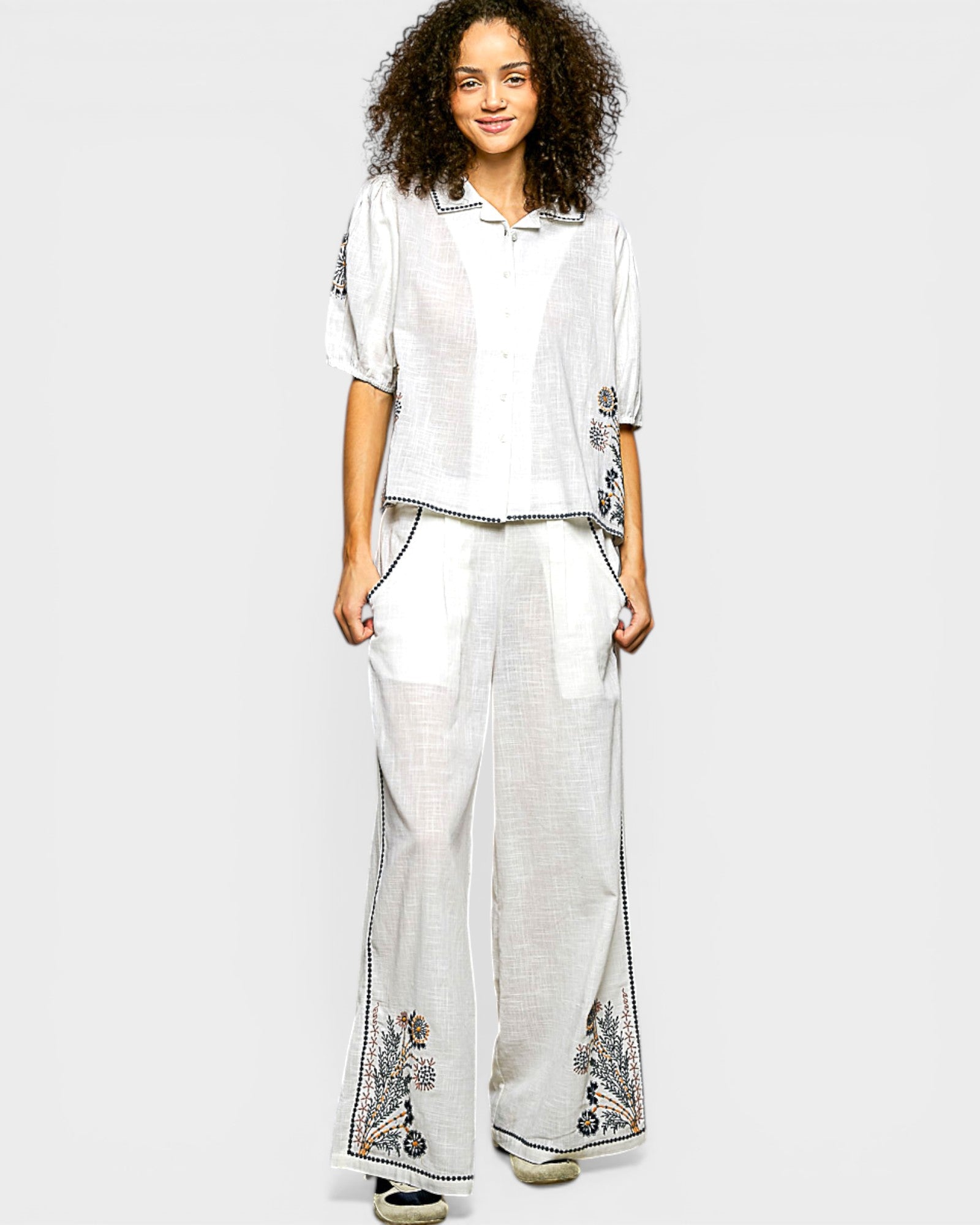 Woman wearing a white outfit with floral embroidery on a plain background