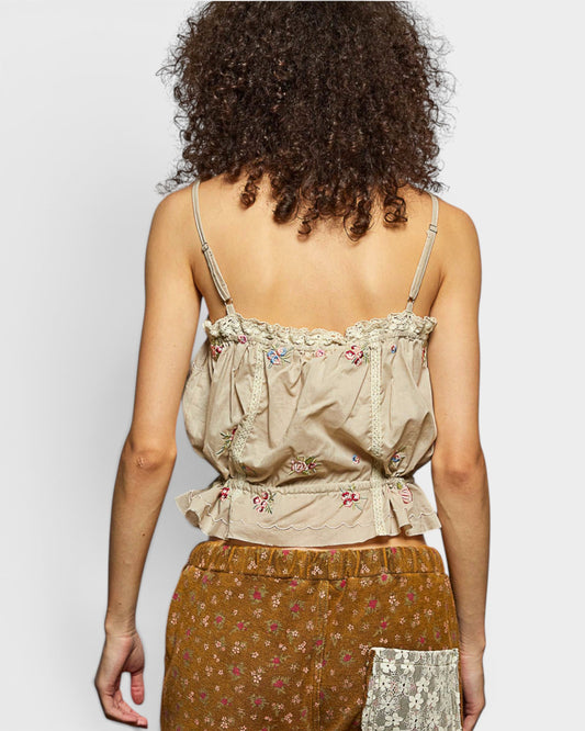 Woman wearing a beige floral top and brown skirt against a plain background