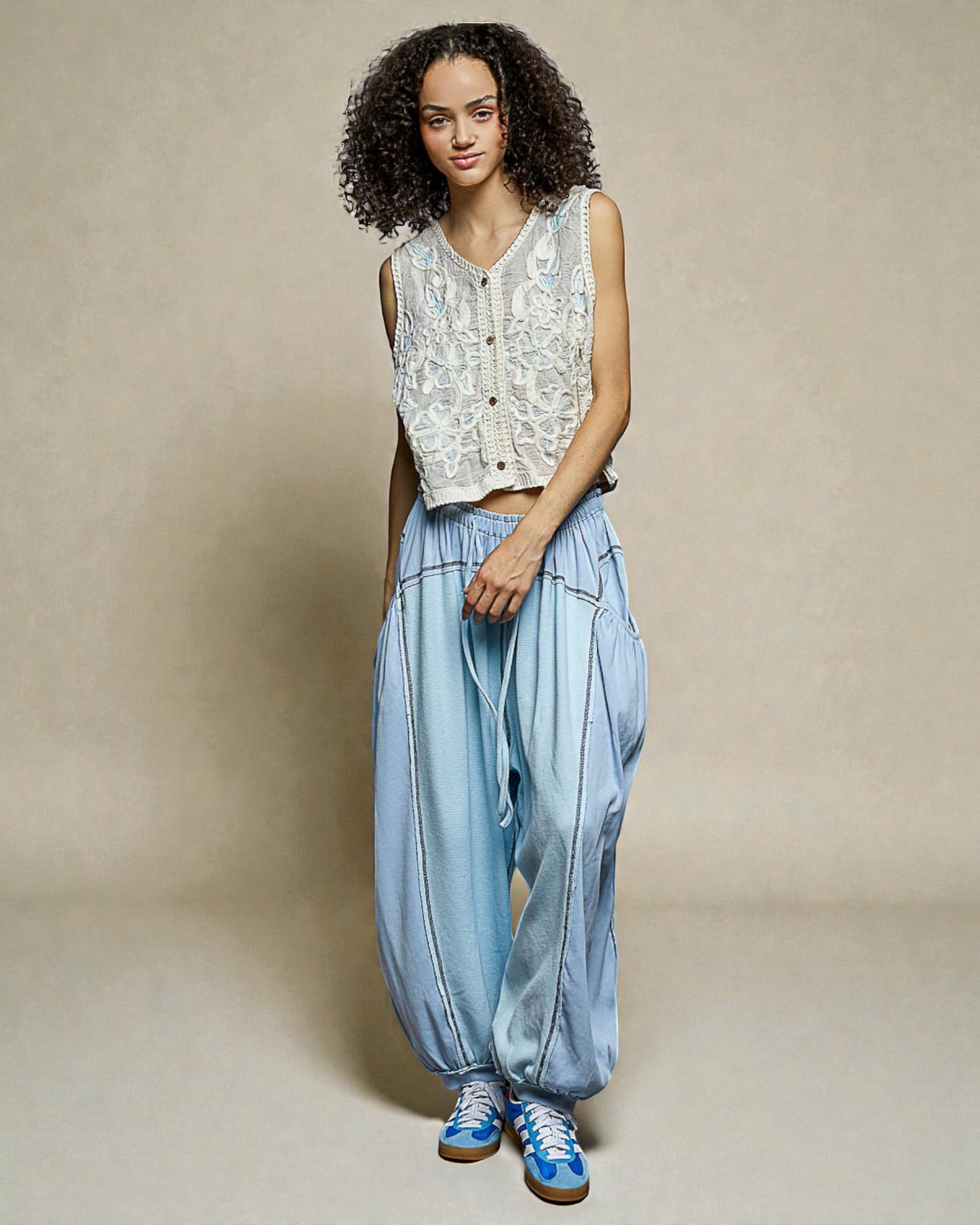 Woman wearing a sleeveless lace top and light blue pants against a beige background
