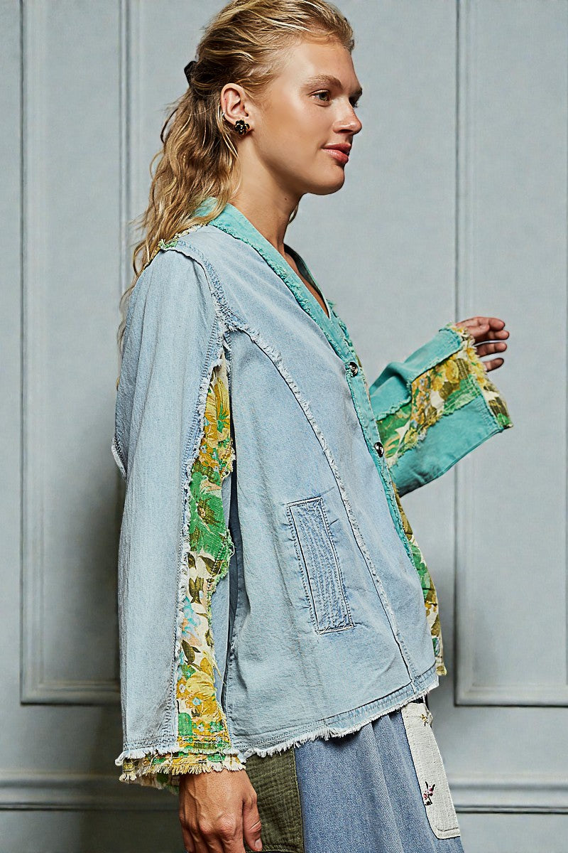 Woman wearing a denim jacket with floral sleeves against a gray wall.