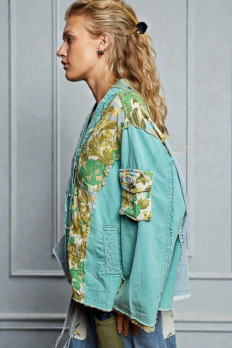 Woman wearing a colorful jacket with floral patterns against a gray wall.