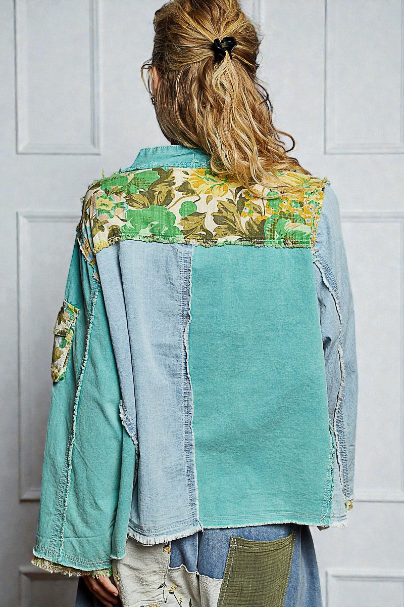 Person wearing a patchwork jacket with floral and denim patterns against a white wall.
