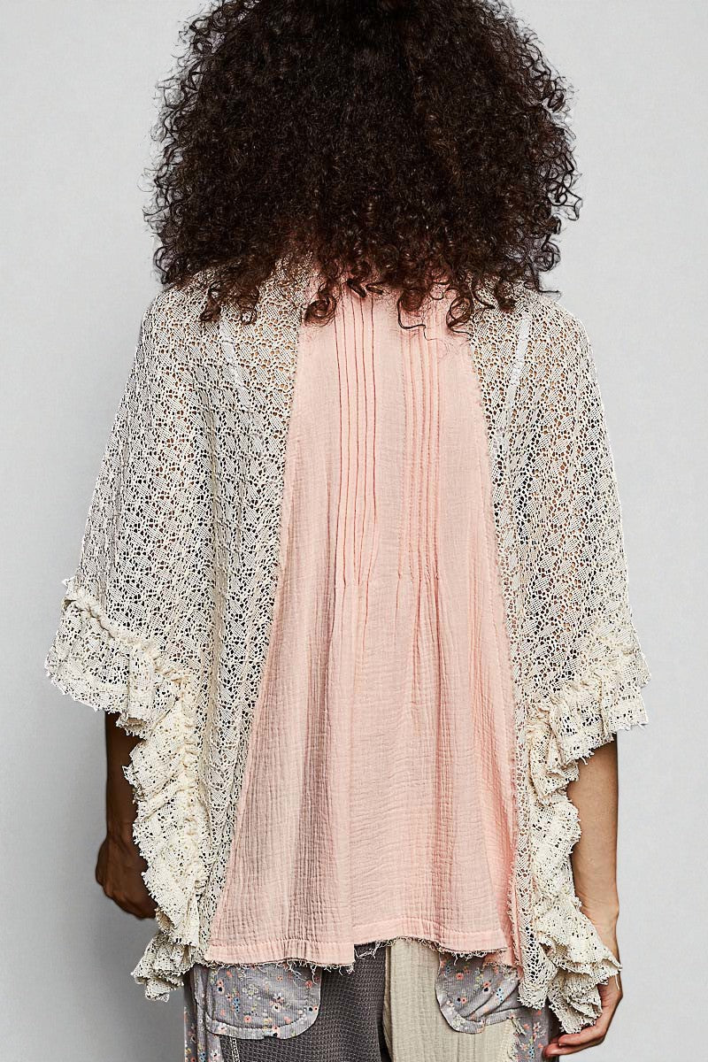 Person wearing a light pink pleated top with a textured beige cardigan against a plain background