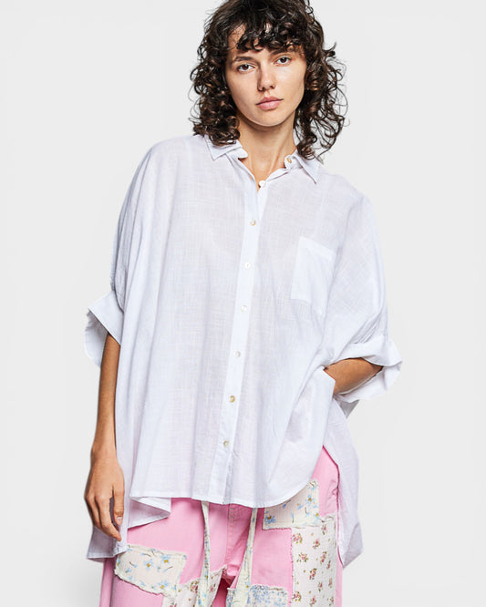 Woman wearing a loose-fitting white shirt with a floral skirt on a plain background