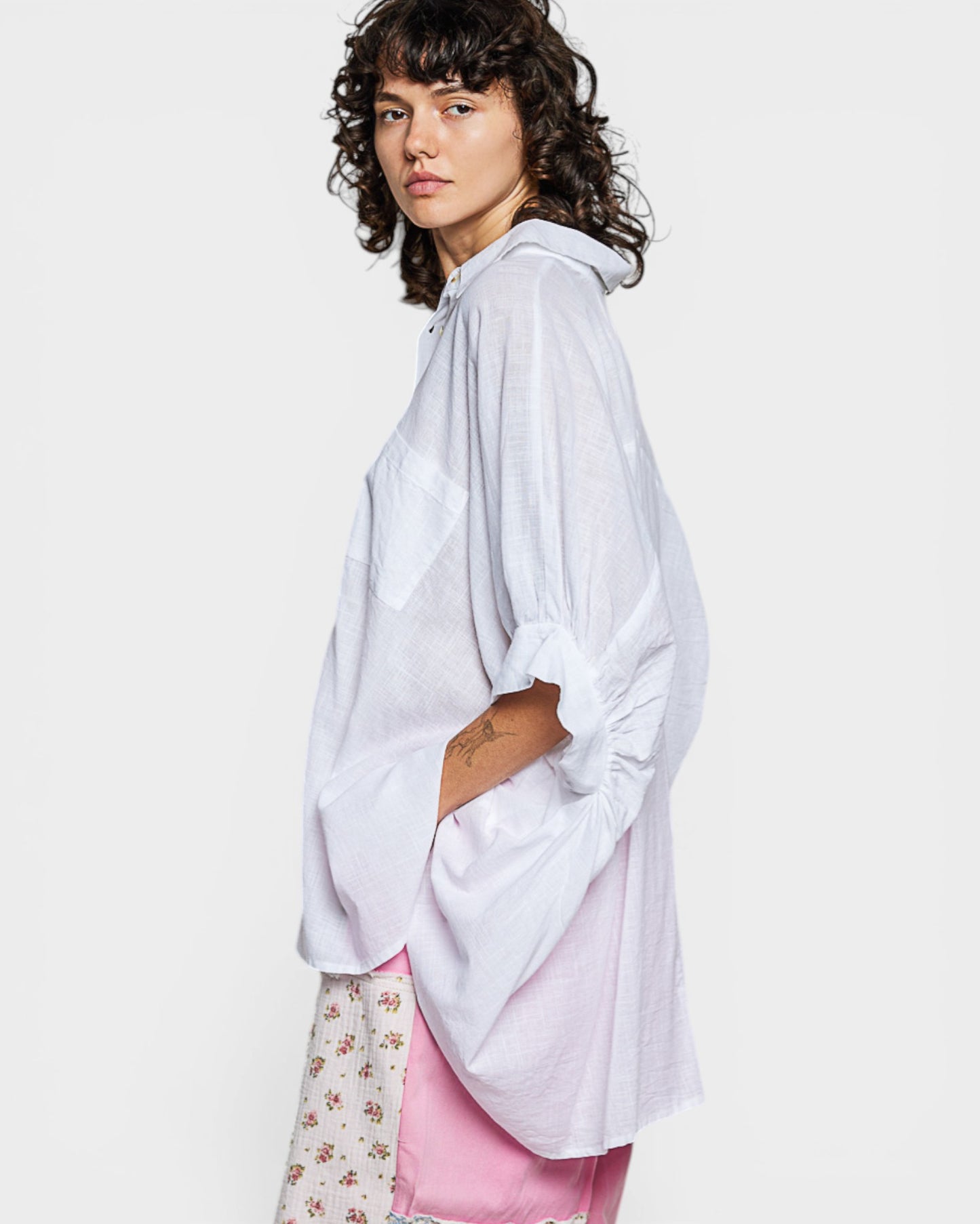 Person wearing a white oversized shirt with floral pants and pink underwear on a plain background