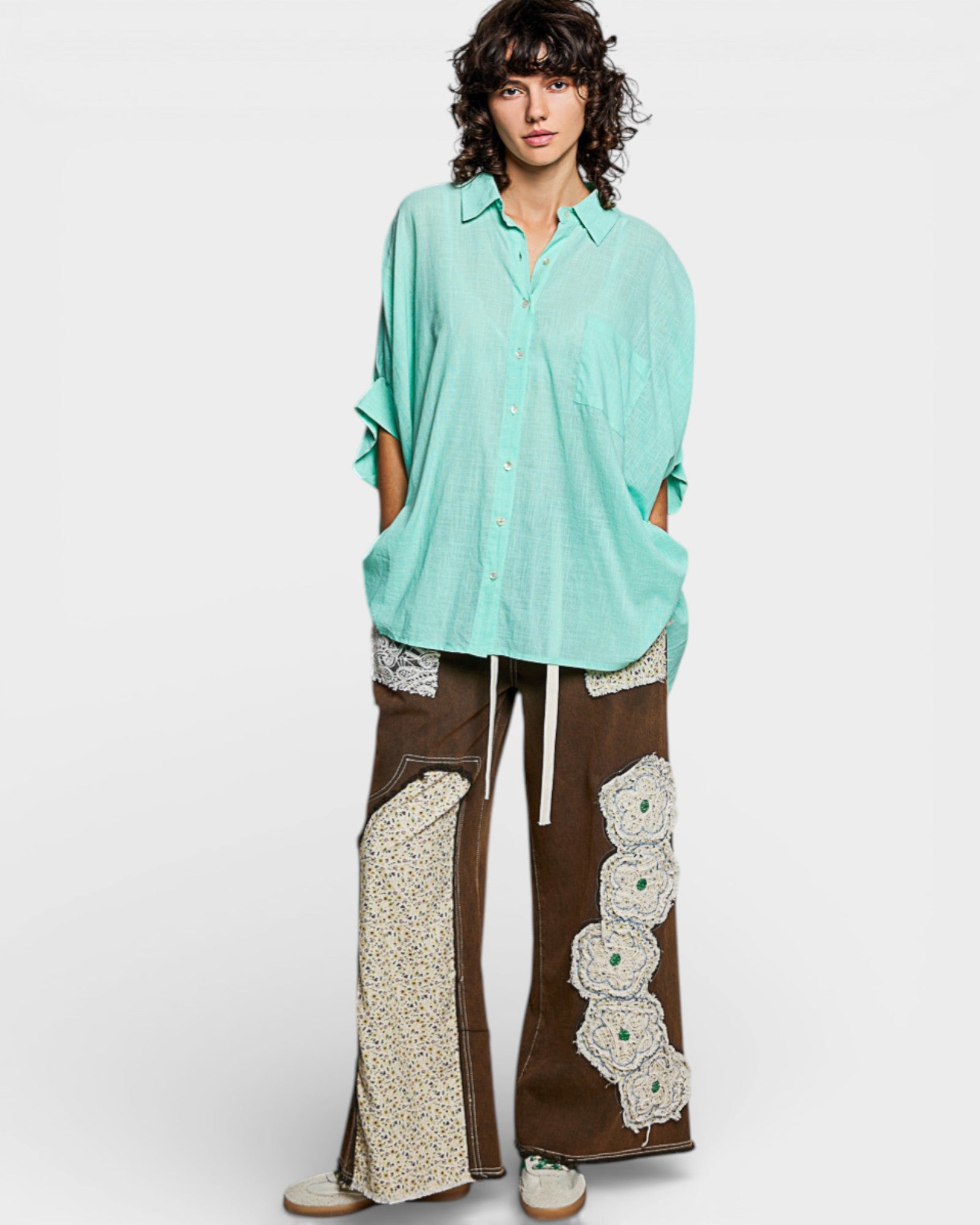 Person wearing a light blue shirt and brown pants with floral patterns on a white background