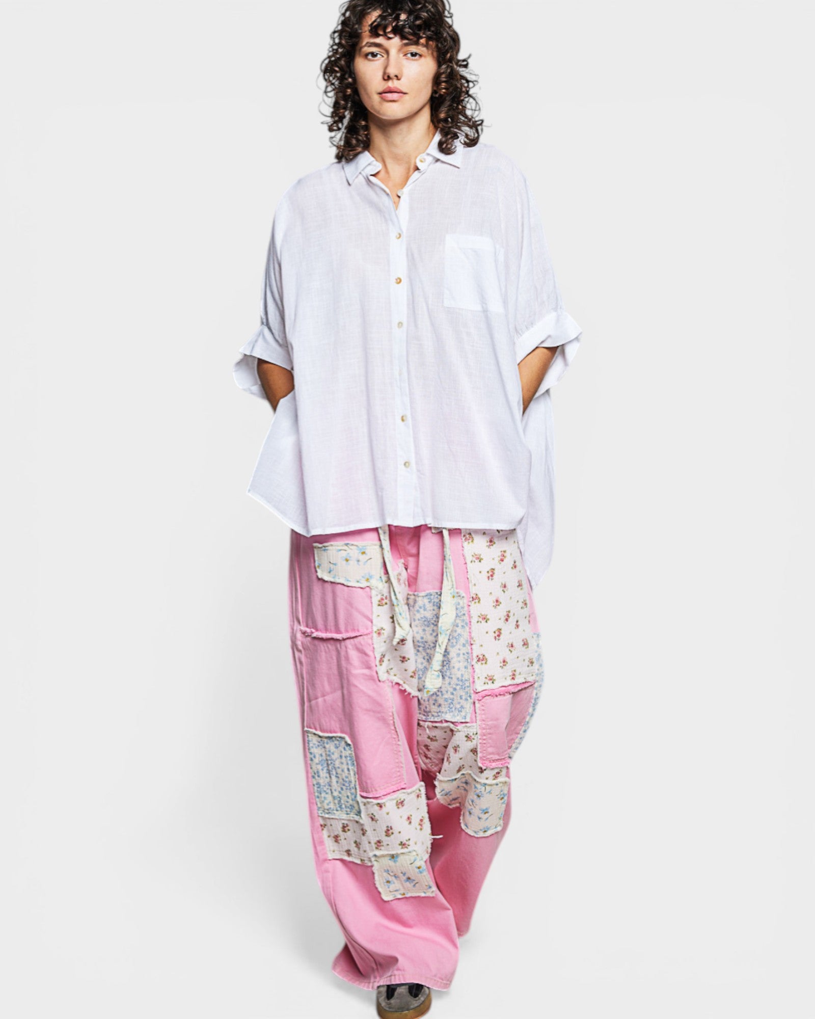 Person wearing a white shirt and pink patchwork pants on a white background