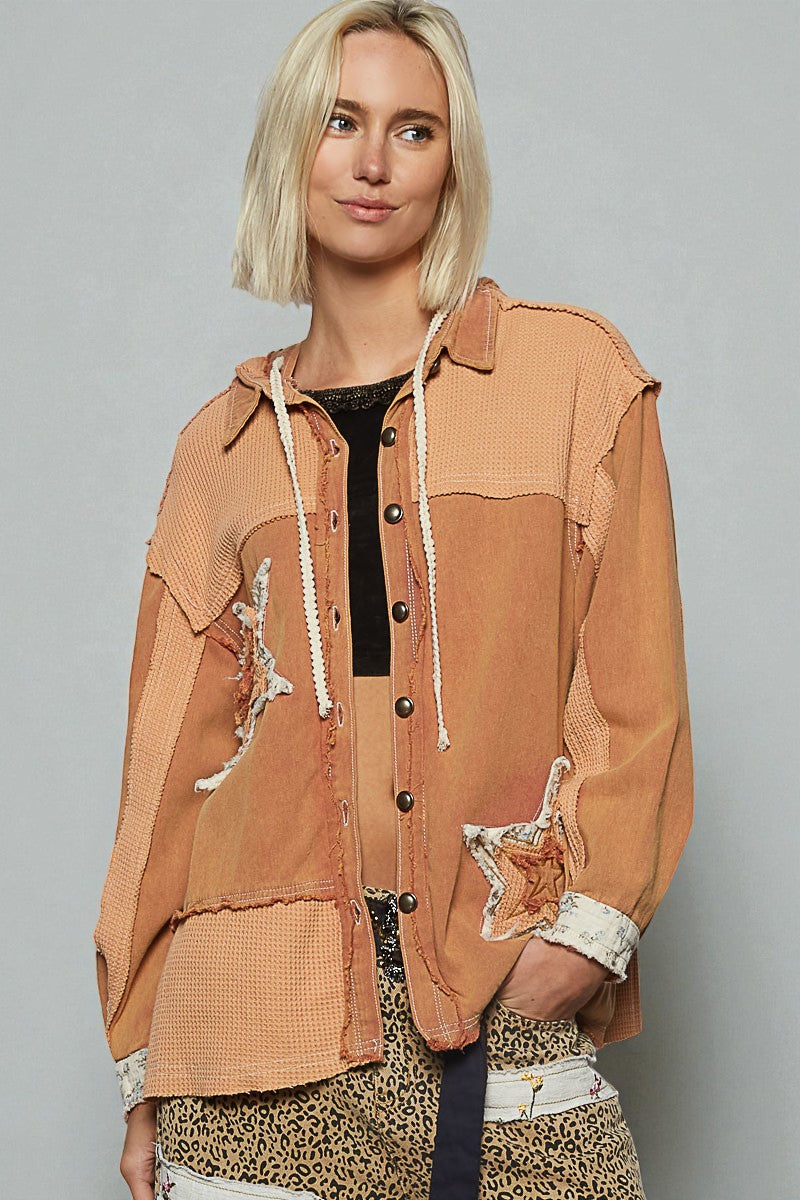 Woman wearing a brown jacket with patchwork design on a gray background