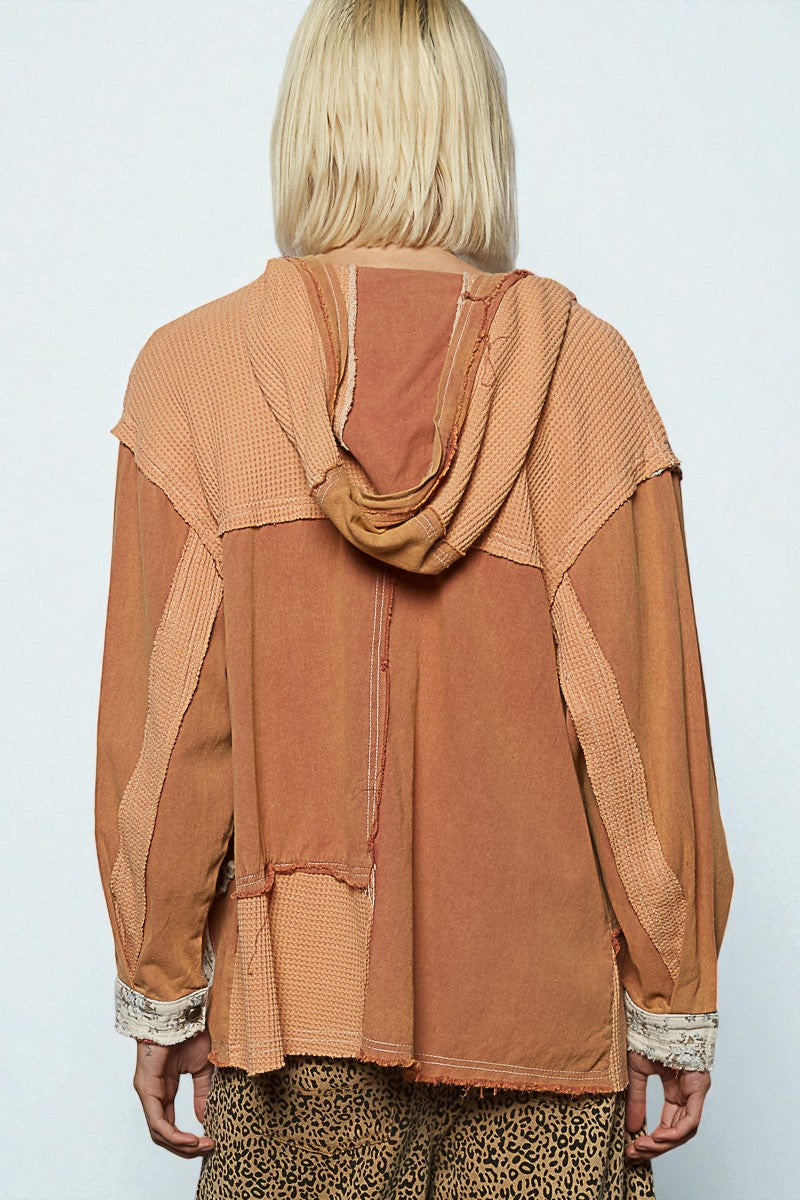 Person wearing a brown layered outfit with a hood against a white background