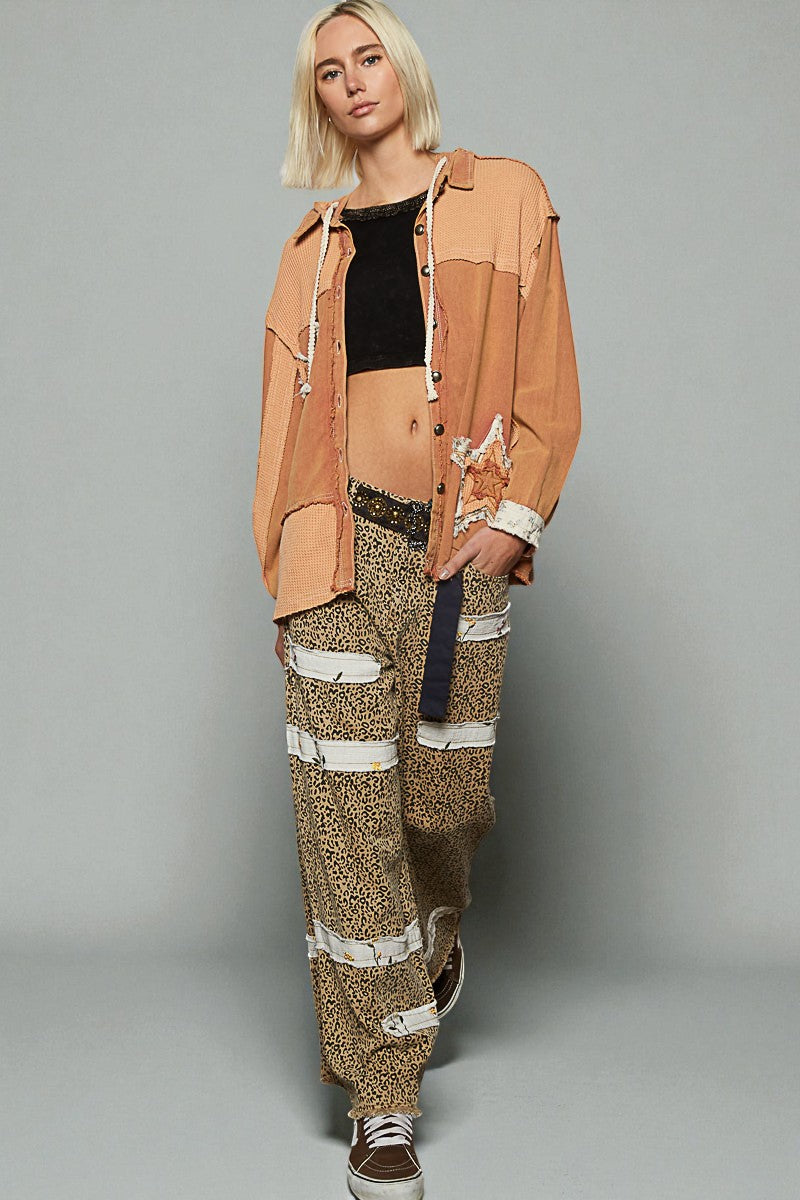 Person wearing a tan jacket and patterned pants on a gray background