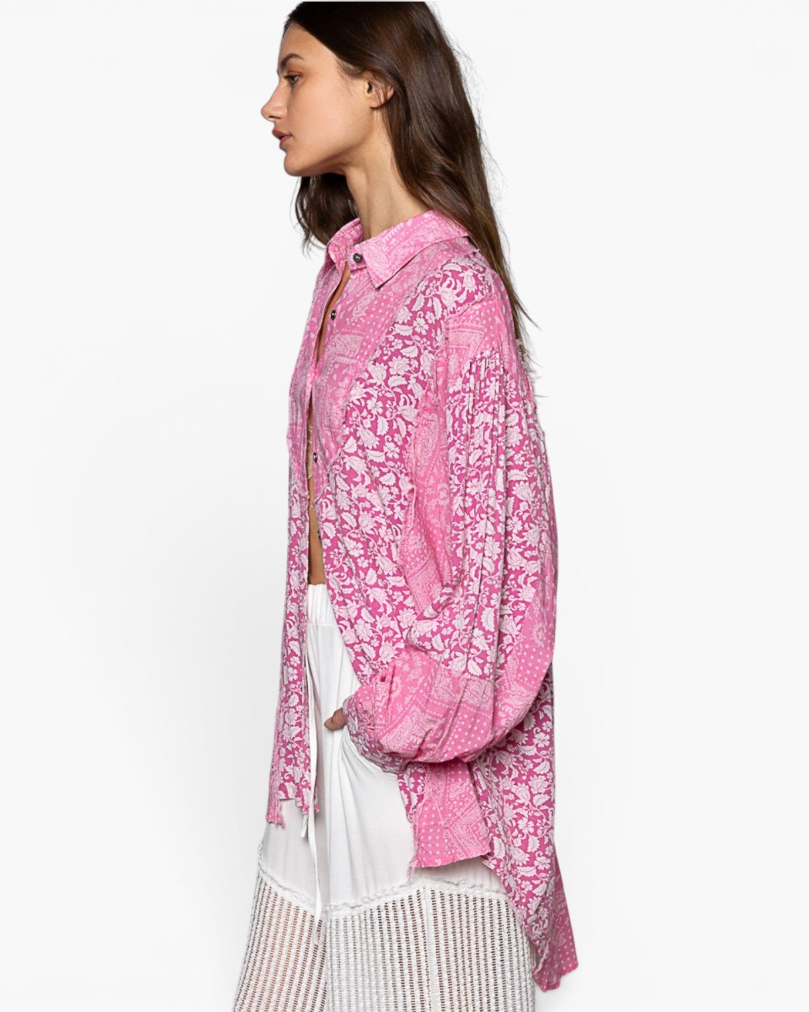 A woman shown in side profile wearing a pink patterned button-up shirt over a white top and white skirt, photographed against a plain light background.