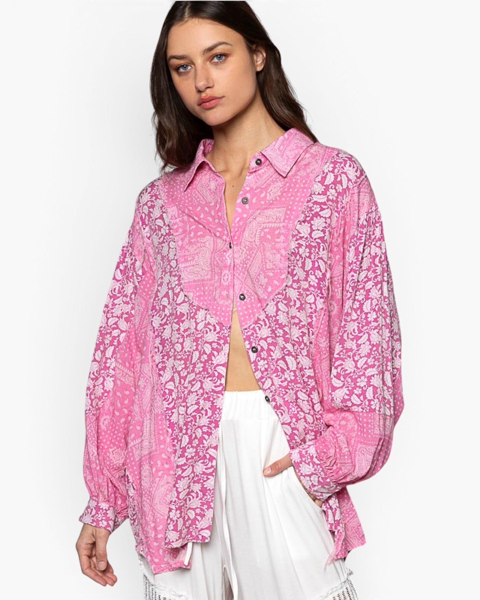 A woman wearing a pink and white patterned button-up shirt with long balloon sleeves, paired with white pants, against a plain white background.