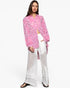 A model wearing a pink floral long-sleeve button-up shirt and white wide-leg sheer crochet pants against a plain white background.