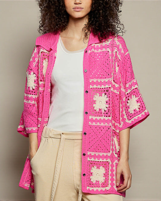 Woman wearing a bright pink embroidered jacket over a white top and beige pants on a neutral background