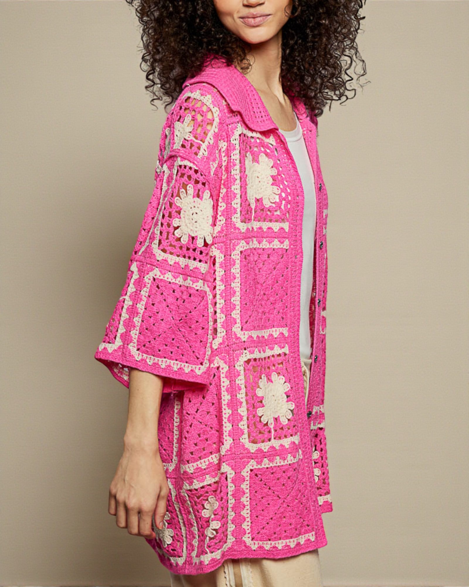 Woman wearing a bright pink crochet jacket with white patterns on a beige background