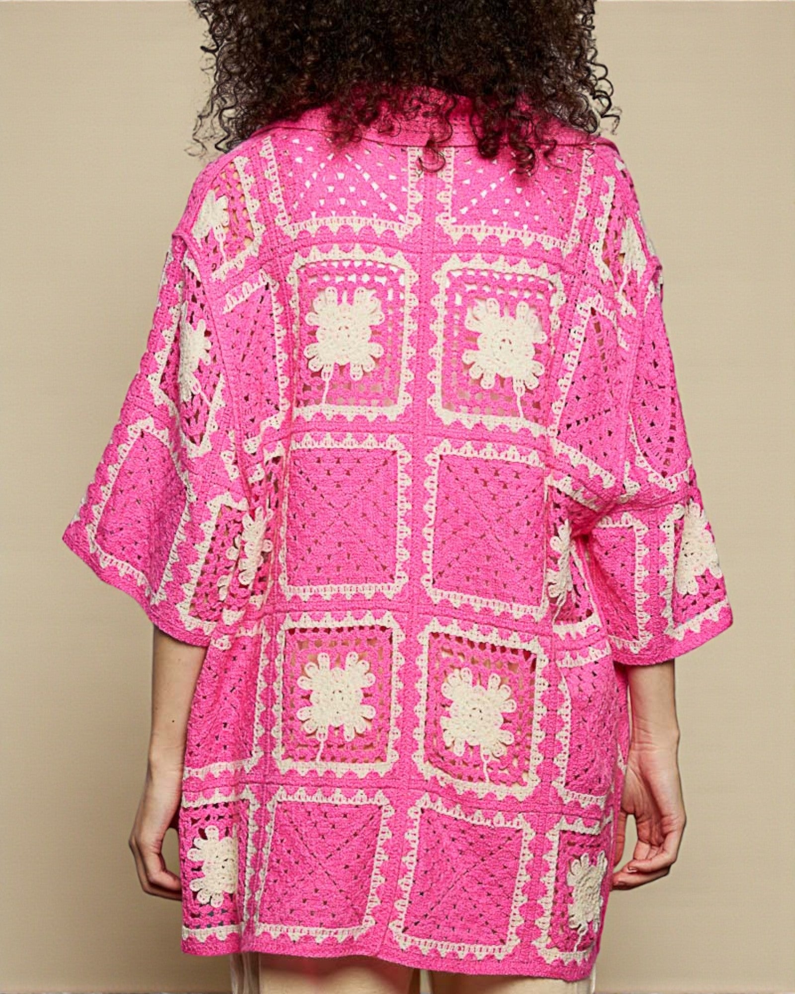Person wearing a bright pink crochet dress with white patterns on a beige background
