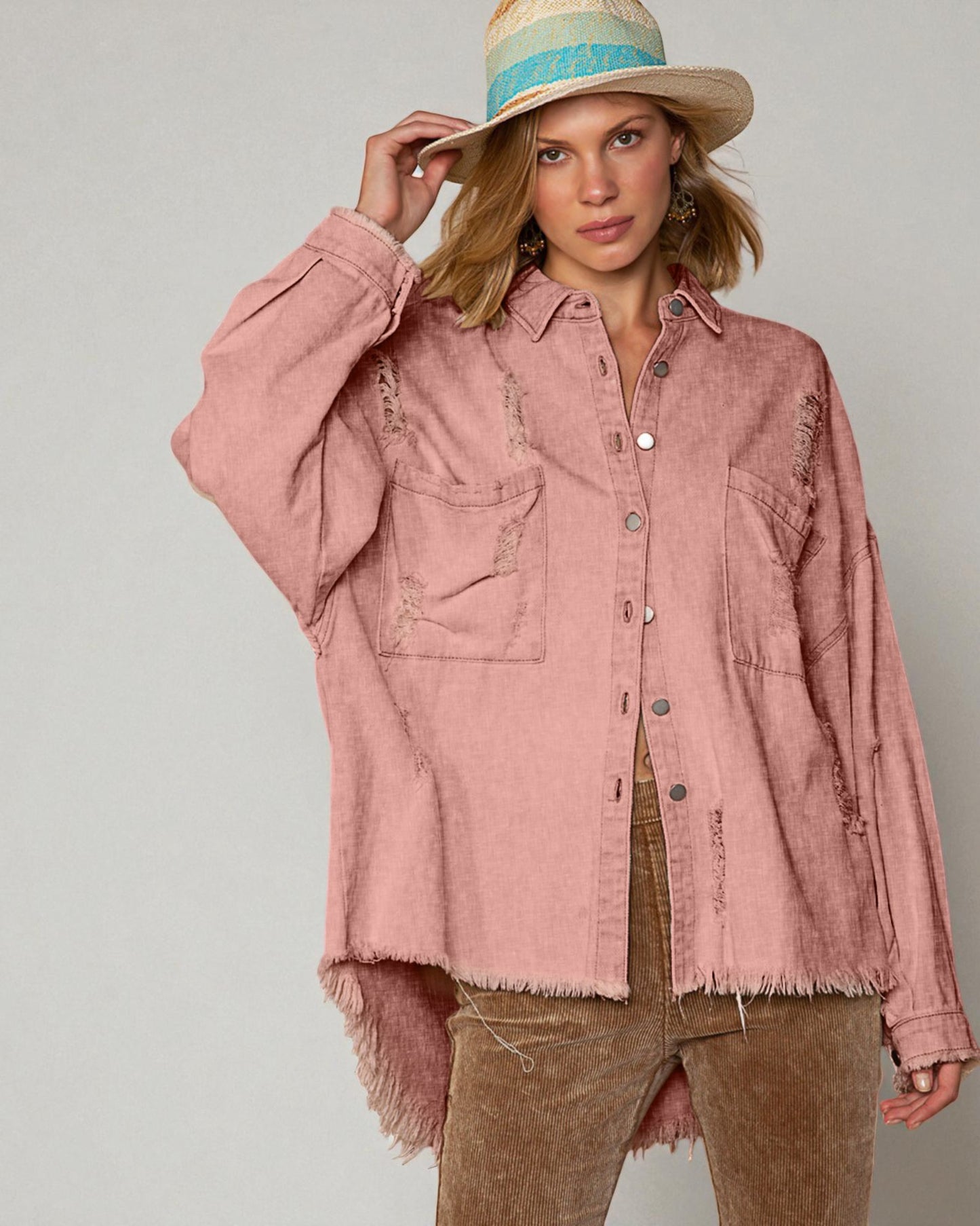 Woman wearing a pink denim jacket and brown pants against a plain background