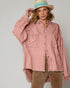 Woman wearing a pink denim jacket and brown pants against a plain background