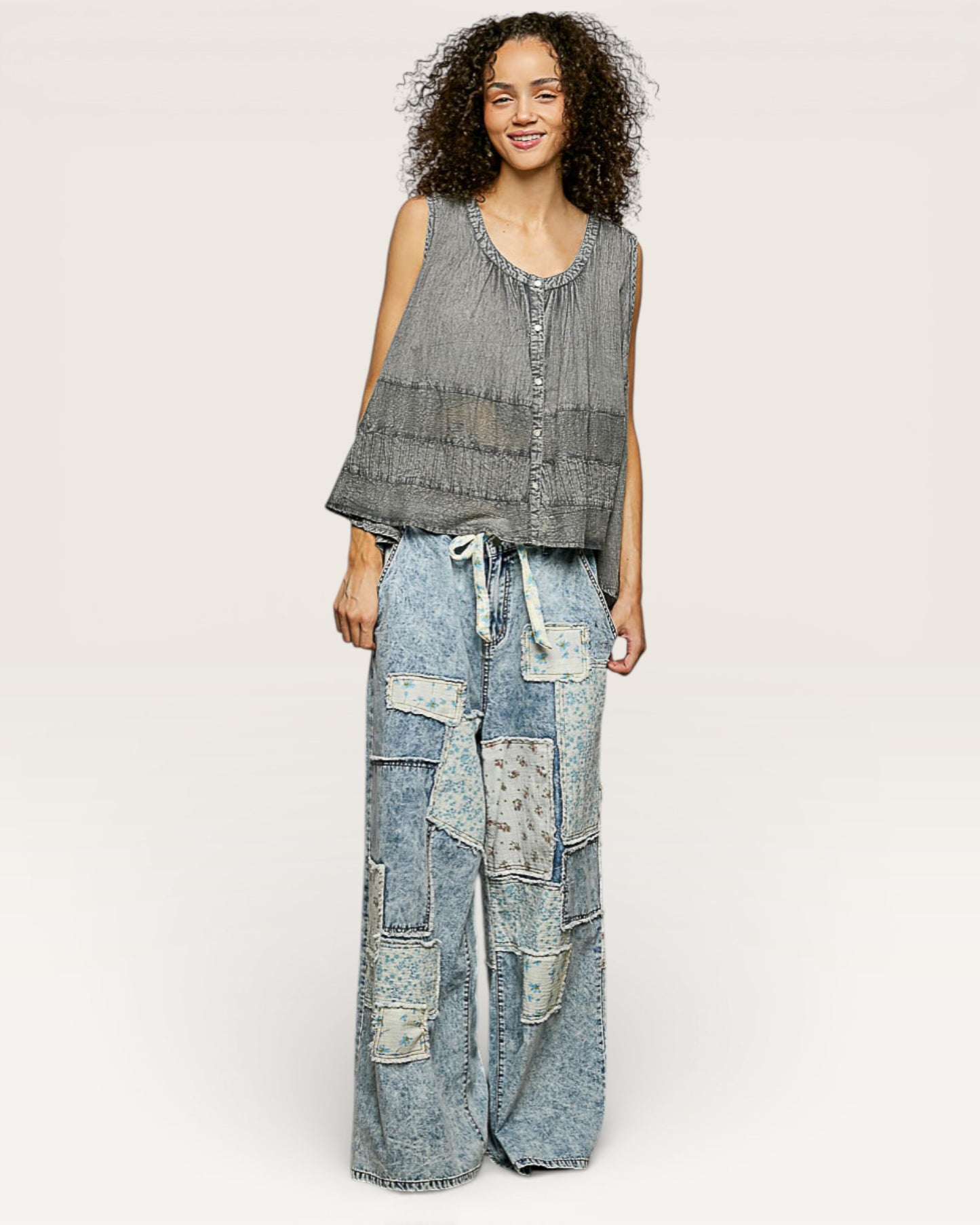 Woman wearing a sleeveless top and patchwork jeans on a white background