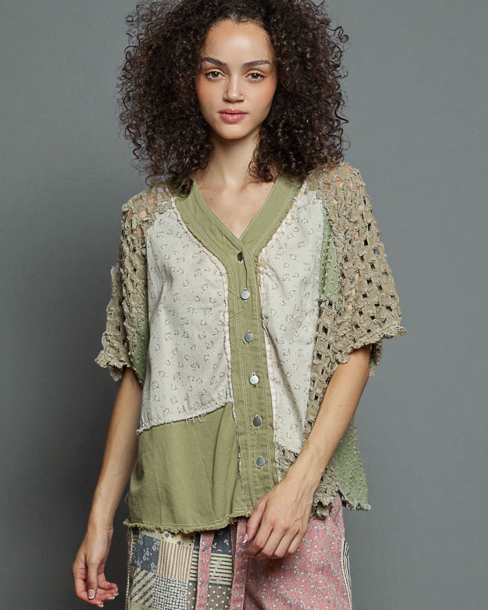 Woman wearing a layered outfit with a textured top and green shirt against a gray background