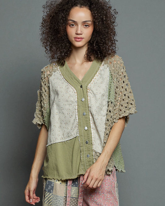 Woman wearing a layered outfit with a textured top and green shirt against a gray background