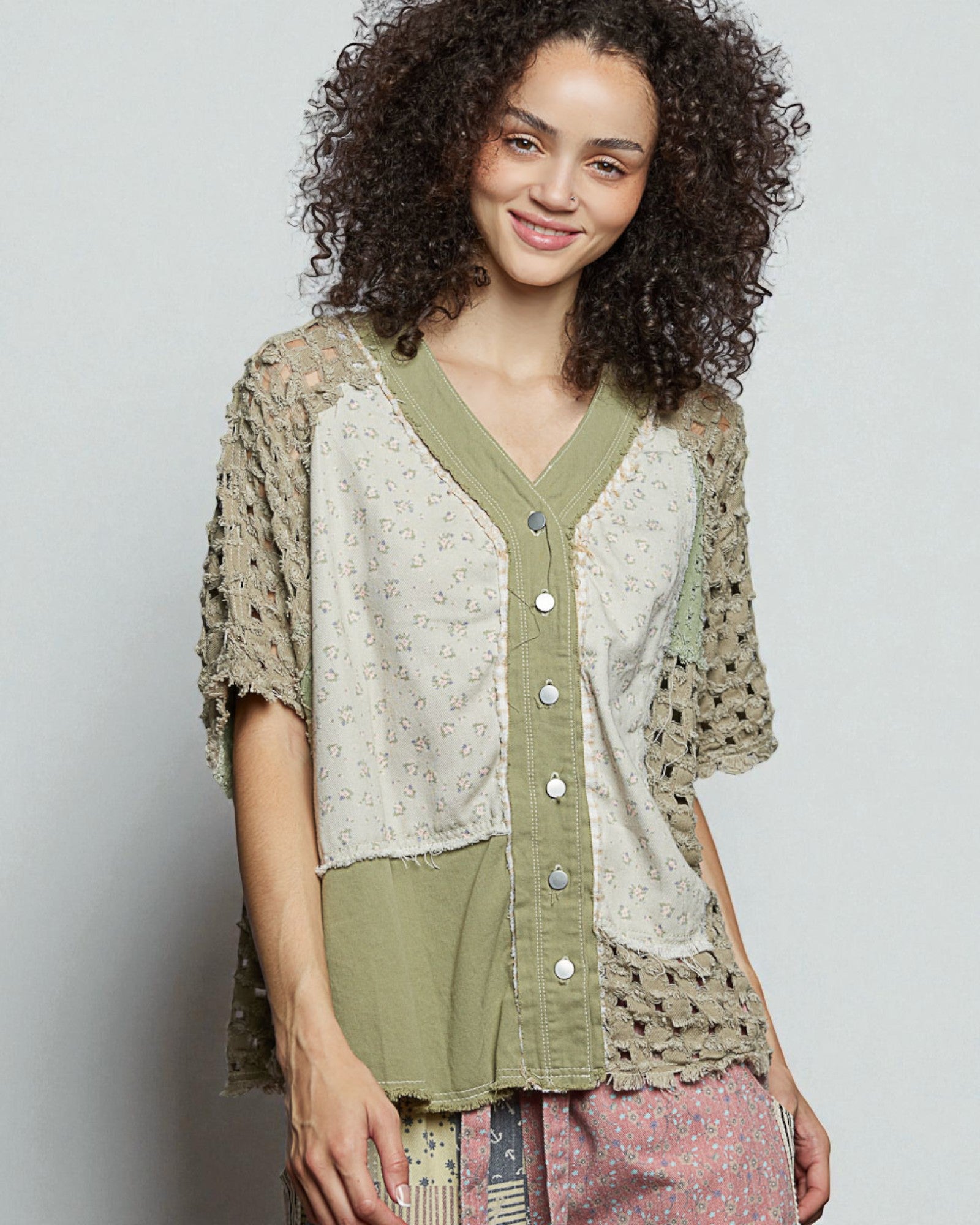 Woman wearing a layered outfit with a patterned top and green cardigan on a plain background