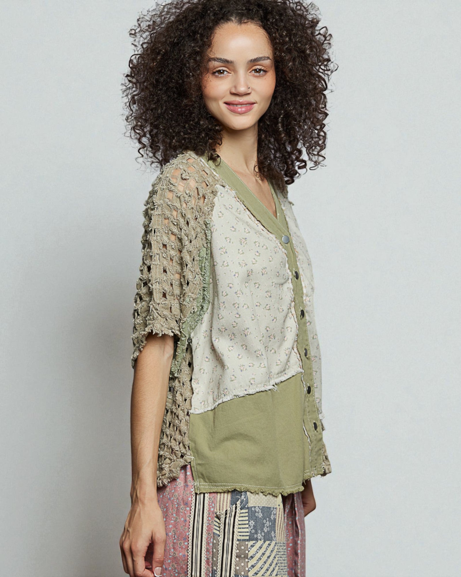 Woman wearing a layered outfit with a textured cardigan and patterned pants against a plain background