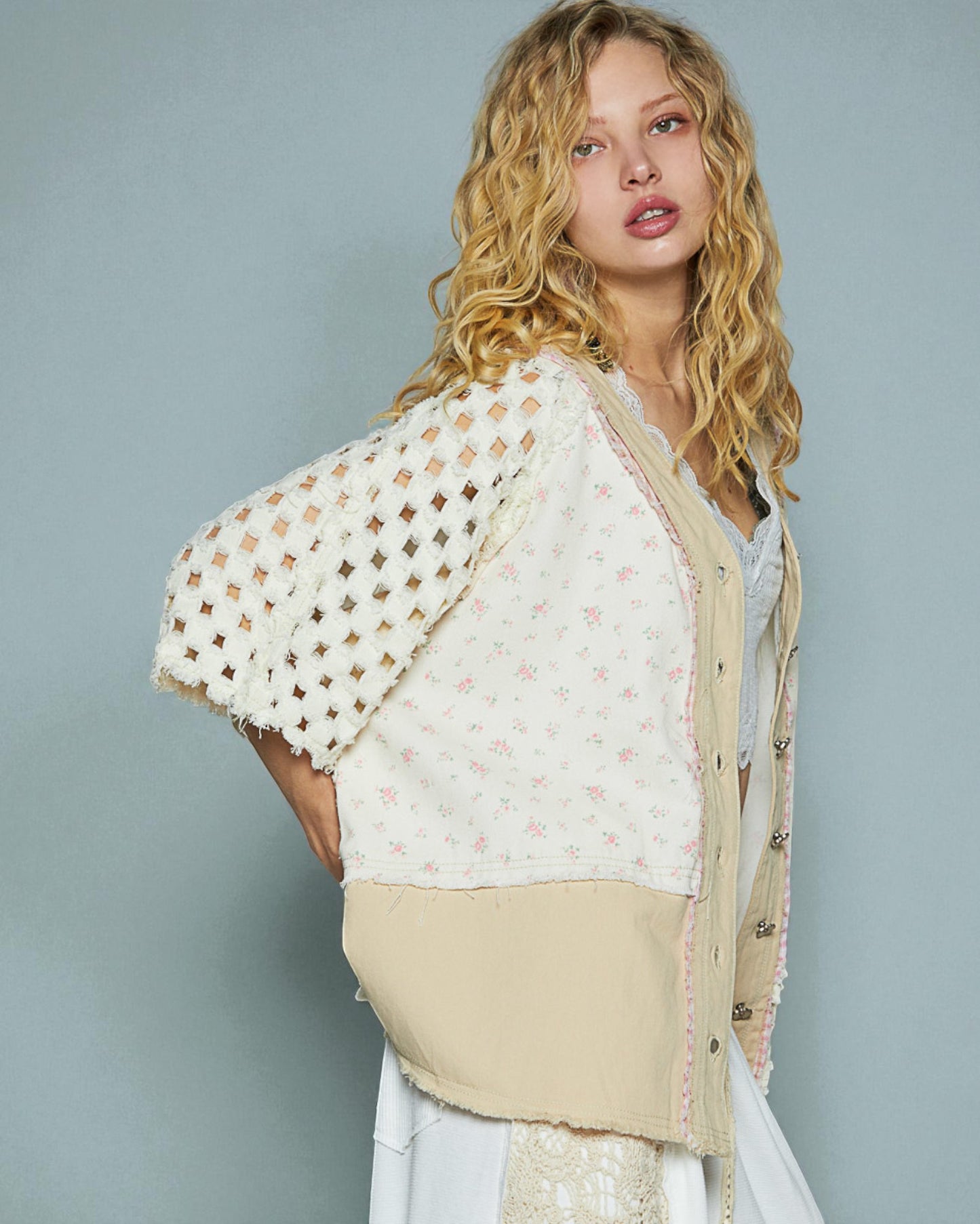 Woman wearing a beige and white outfit with a textured shawl against a gray background
