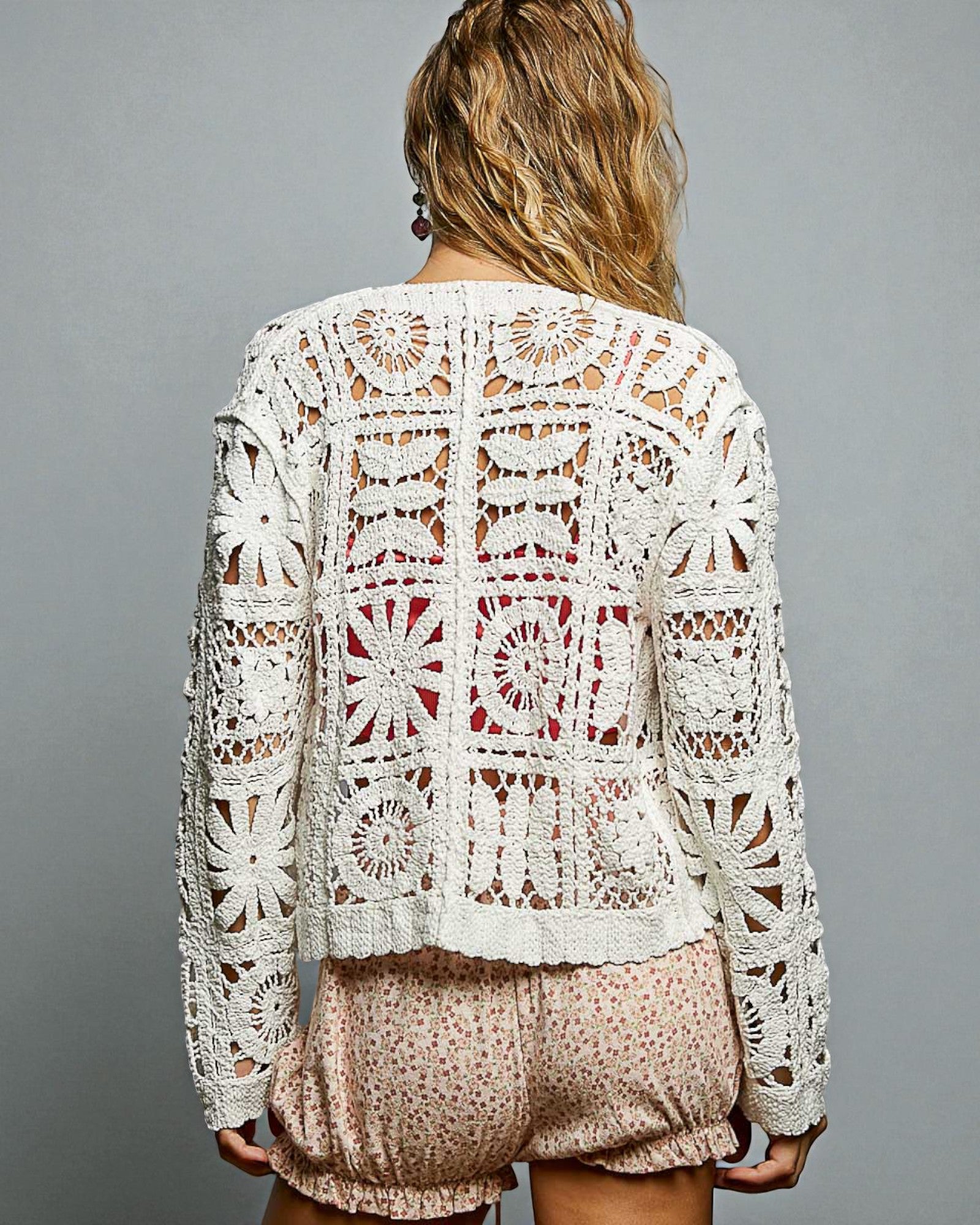 Woman wearing a white crochet top and pink shorts against a gray background