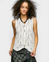 Woman wearing a white sleeveless top with black buttons on a plain background