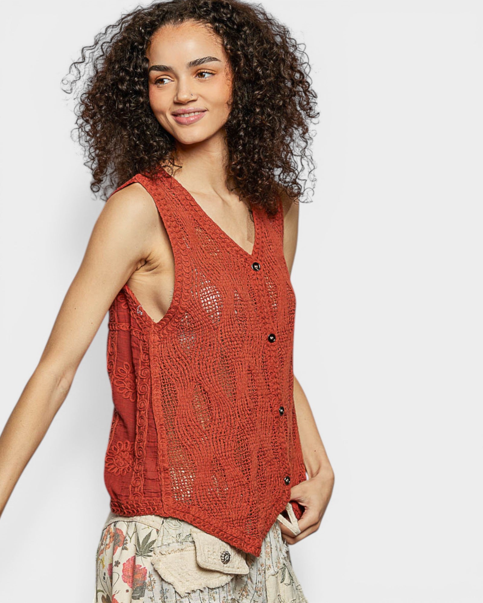 Woman wearing a red sleeveless knitted top with black buttons on a white background