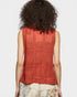 Person wearing a red sleeveless top with intricate patterns on a plain background