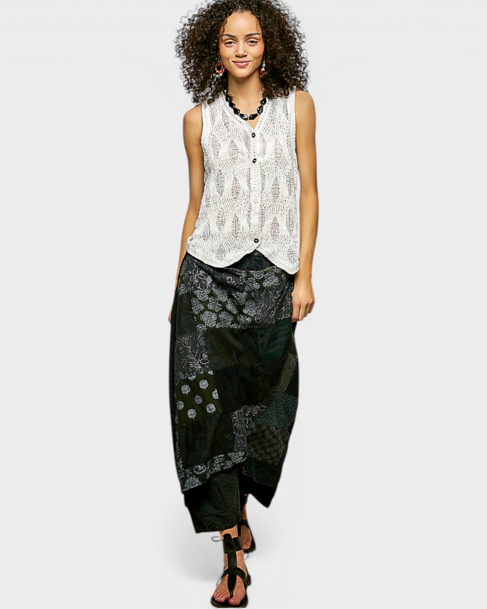 Woman wearing a sleeveless patterned top and black pants on a white background