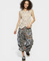 Woman wearing a sleeveless patterned top and floral harem pants on a white background