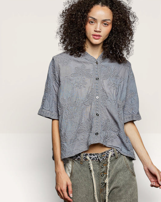 Woman wearing a gray patterned shirt with rolled-up sleeves on a plain background