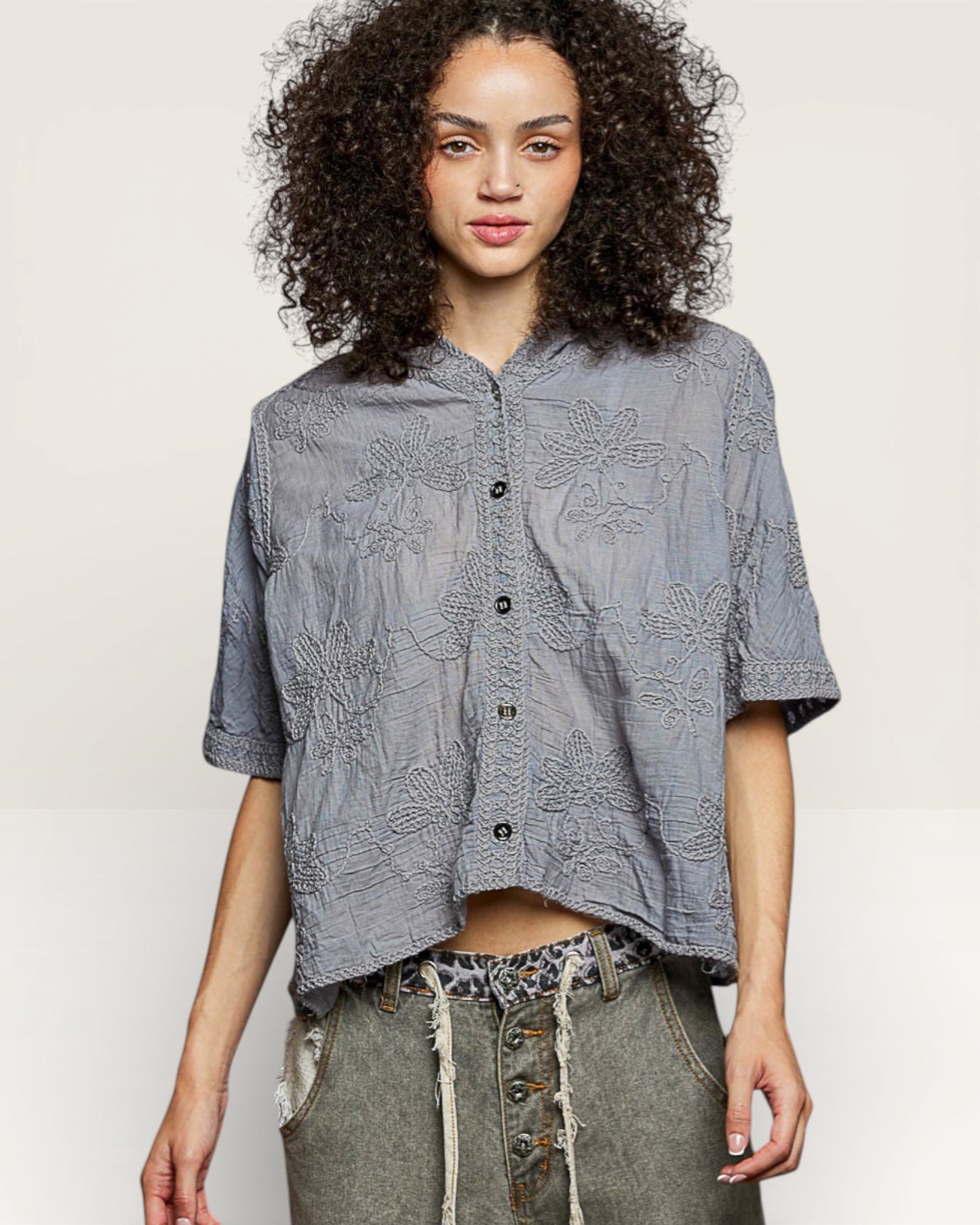 Woman wearing a gray patterned shirt with rolled-up sleeves on a plain background