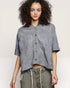 Woman wearing a gray patterned shirt with rolled-up sleeves on a plain background
